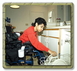 A woman in a wheelchair emptying the dishwasher in her home, which has environmental and architechtural elements htat enable her to function normally.